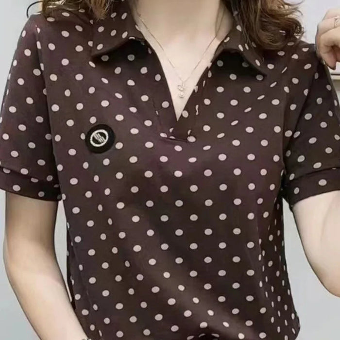 A close-up of a woman wearing a dark brown short-sleeve polo shirt with a white polka dot pattern. The shirt features a collar, a partial button placket, and a small black circular patch on the left chest.