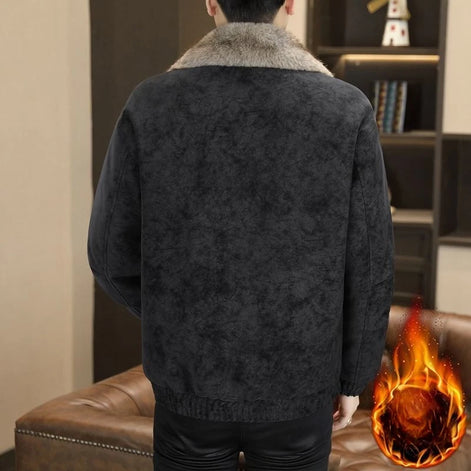 A man viewed from the back wearing a dark charcoal textured jacket with a thick light gray faux-fur collar, standing in an indoor room with a brown leather sofa 
