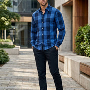 A man wearing a long-sleeve button-up shirt with a bold blue and navy buffalo plaid pattern, standing in an office environment.