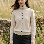 A person wearing a light beige ribbed turtleneck cardigan sweater with black buttons, photographed in a cafe setting. The text 'WinvyNee' is overlaid in the top left corner.