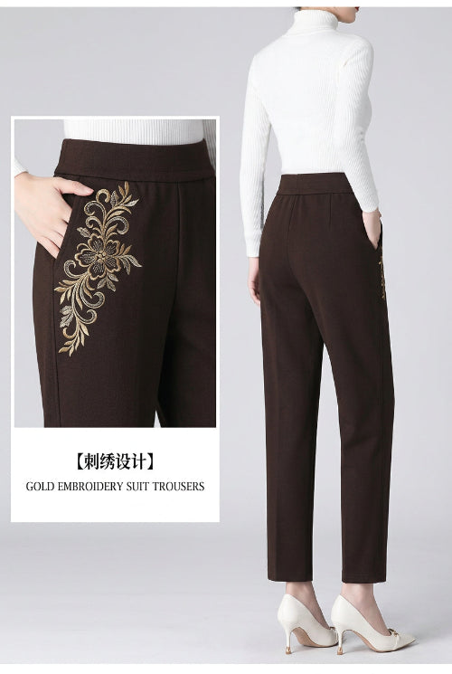 Dark brown suit trousers shown on a model, featuring a wide elastic waistband, side pockets, and a small gold embroidered bee detail on the left leg. 