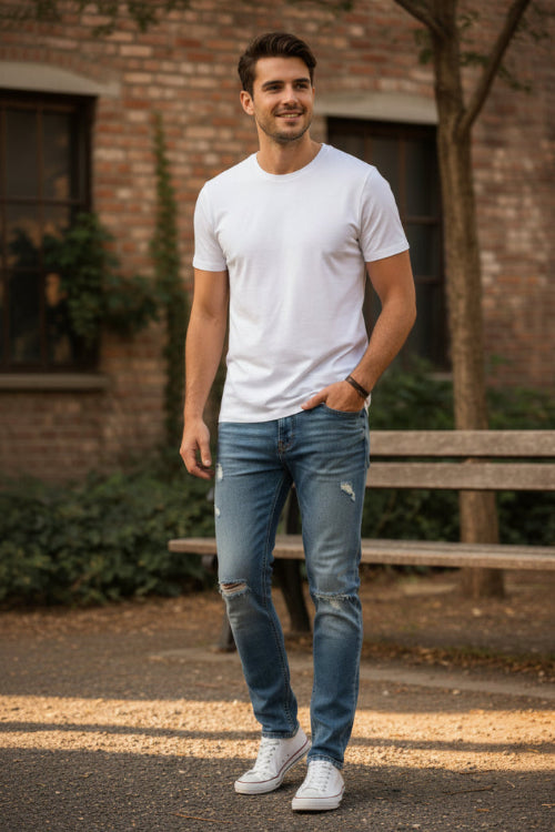 Person wearing distressed blue jeans and white sneakers on a grassy background