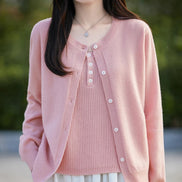 A woman wearing a light pink open-front cardigan over a matching pink ribbed top, photographed outdoors with a softly blurred green background.