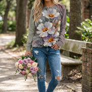 A woman wearing a long-sleeve crewneck sweatshirt with a large, colorful floral print on the front and solid taupe sleeves, paired with blue jeans.