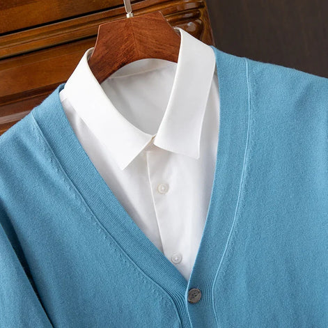 Blue cardigan over a white shirt on a wooden hanger against a dark background