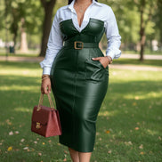 Woman in a green dress and white shirt holding a red handbag in an indoor setting.