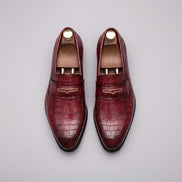 Pair of maroon loafers with gold accents on a grid background