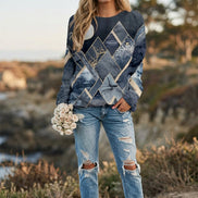 A woman wearing a long-sleeve crewneck sweatshirt with a blue and beige mountain and tree pattern, paired with blue jeans.