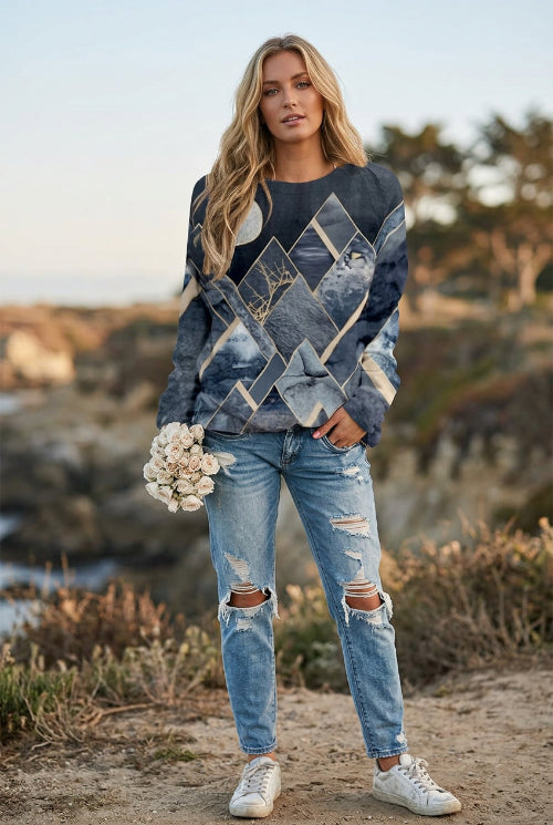 A woman wearing a long-sleeve crewneck sweatshirt with a blue and beige mountain and tree pattern, paired with blue jeans.