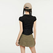 A model shown from behind wearing a black short-sleeve textured polo shirt and an olive green mini skirt, paired with a beige baseball cap.