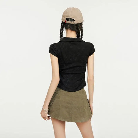 A model shown from behind wearing a black short-sleeve textured polo shirt and an olive green mini skirt, paired with a beige baseball cap.