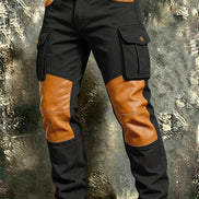 Black cargo pants with tan contrast panels at the knees and front pockets, flap thigh pockets, and a brown belt against a textured gray background.