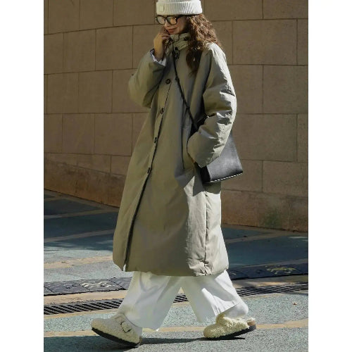 Woman walking outdoors in an army green long padded coat with a buttoned stand collar, white wide-leg trousers and a black shoulder bag