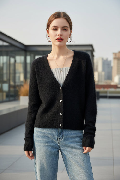 A person wearing a dark fuzzy knit cardigan over a light gray top and light blue jeans, 