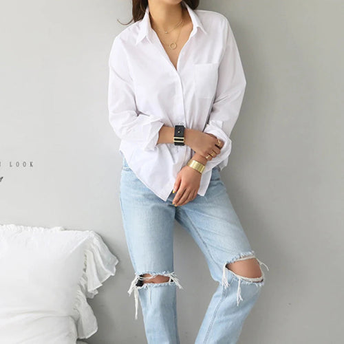 White long-sleeve button-down shirt worn by a model standing in ripped jeans.