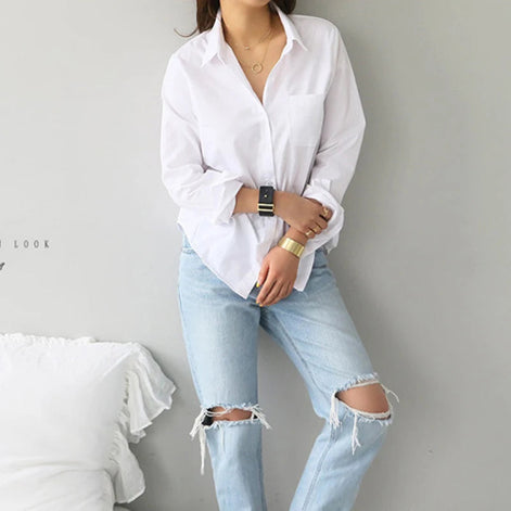 White long-sleeve button-down shirt worn by a model standing in ripped jeans.