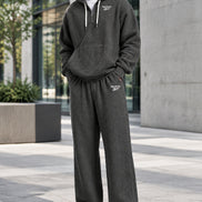 A man wearing a dark gray waffle-knit hoodie and matching sweatpants set with white Reebok logos, shown against a plain white background.