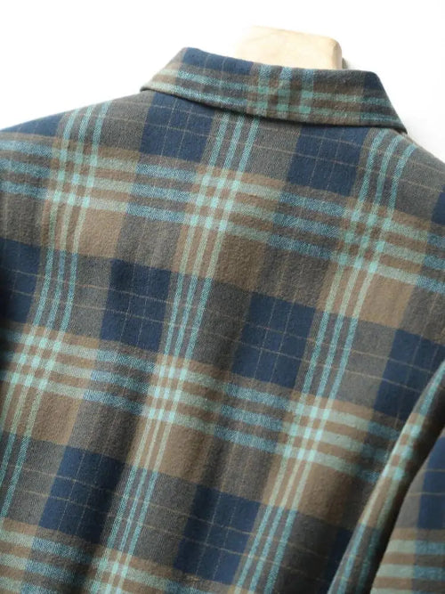 A close-up of a plaid flannel shirt on a mannequin, featuring a pattern of navy blue, brown, and light blue stripes.