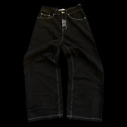 Front view of black wide-leg jeans laid flat, showing white contrast stitching, front pockets, belt loops, and a small white graphic on the fly.