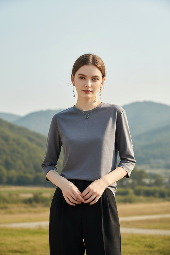 Person wearing a gray long-sleeve shirt and black pants against a neutral background