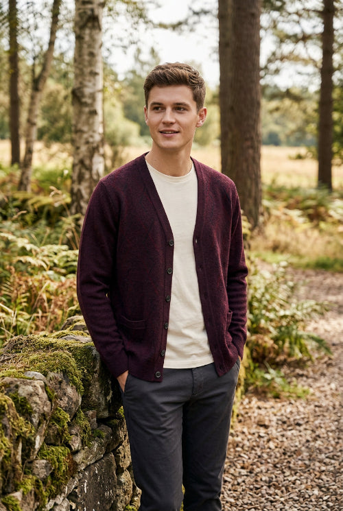A men's knit cardigan sweater in a deep plum purple color, hanging on a wooden hanger against a white background. The cardigan features a V-neck, button-up front, and two front patch pockets.