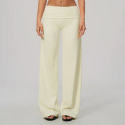 A model from the waist down wearing light cream wide-leg lounge pants with a wide waistband, paired with black slide sandals, against a light gray studio background.