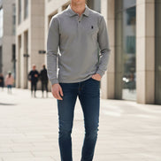 Gray polo shirt with a brand logo held by a hand, on a hanger against a blurred background.