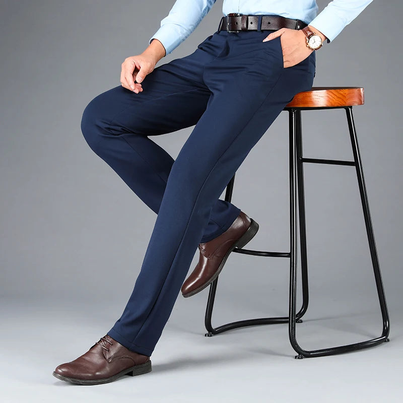 Person wearing navy blue pants and brown shoes sitting on a bar stool against a gray background