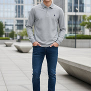 Gray polo shirt with Ralph Lauren logo held by a hand, with more shirts in the background.