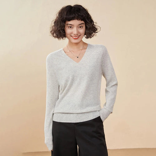 Woman wearing a light gray sweater and black pants against a beige background
