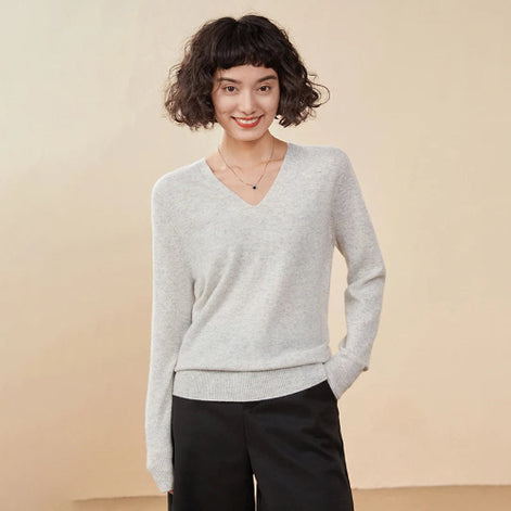 Woman wearing a light gray sweater and black pants against a beige background