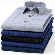 A stack of neatly folded long-sleeve dress shirts in various blue and navy tones, including a light gray shirt with a subtle plaid pattern on top, set against a plain white background.
