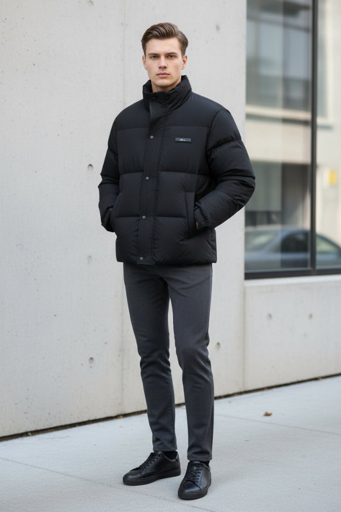 A black puffer jacket hanging on a clothing rack in a retail store setting, with promotional graphic overlays on the left highlighting warmth, softness, and down content. The jacket has a high collar, front zipper and snap closure, and a small chest label.