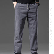 A person wearing dark gray drawstring sweatpants with a black long-sleeve top and white sneakers, shown from the chest down against a dark gray studio background.