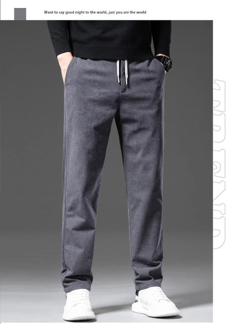 A person wearing dark gray drawstring sweatpants with a black long-sleeve top and white sneakers, shown from the chest down against a dark gray studio background.
