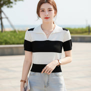 A woman wearing a short-sleeve knit polo shirt with bold black and off-white horizontal stripes, seated on a dark brown leather couch and holding a magazine.