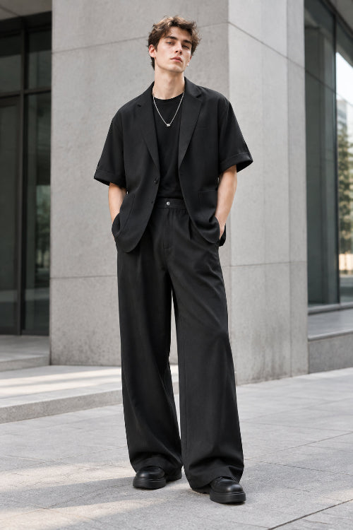 A two-piece men's casual outfit set in black, featuring a short-sleeve blazer-style jacket with rolled sleeves and a matching pair of wide-leg trousers, 