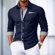 Man wearing a navy button-up shirt with light gray trim and white pants against a blurred background