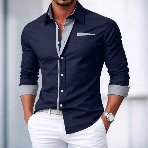 Man wearing a navy button-up shirt with light gray trim and white pants against a blurred background