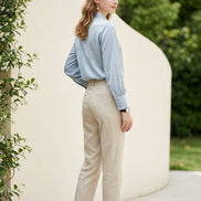 Woman wearing a light gray blouse with long sleeves against a neutral background