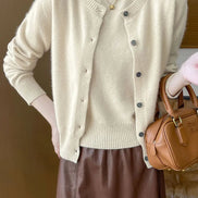 A person wearing a cream-colored knit cardigan with dark buttons, paired with a brown skirt and holding a brown leather handbag.