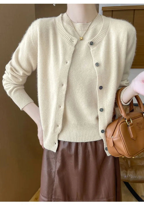 A person wearing a cream-colored knit cardigan with dark buttons, paired with a brown skirt and holding a brown leather handbag.
