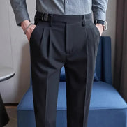 Person wearing dark gray pleated pants and a light gray shirt in a room with a blue chair.