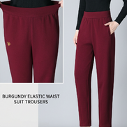 A model wears high-waisted burgundy suit pants with side pockets, paired with black heels. The image includes a close-up inset of the pants'