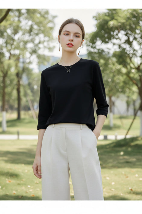 Person wearing a black t-shirt and white pants sitting on a wooden floor.