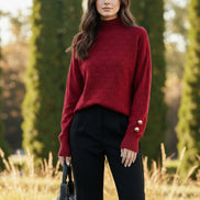 A woman wearing a red ribbed turtleneck sweater with a textured checkerboard pattern on the chest and sleeves, 