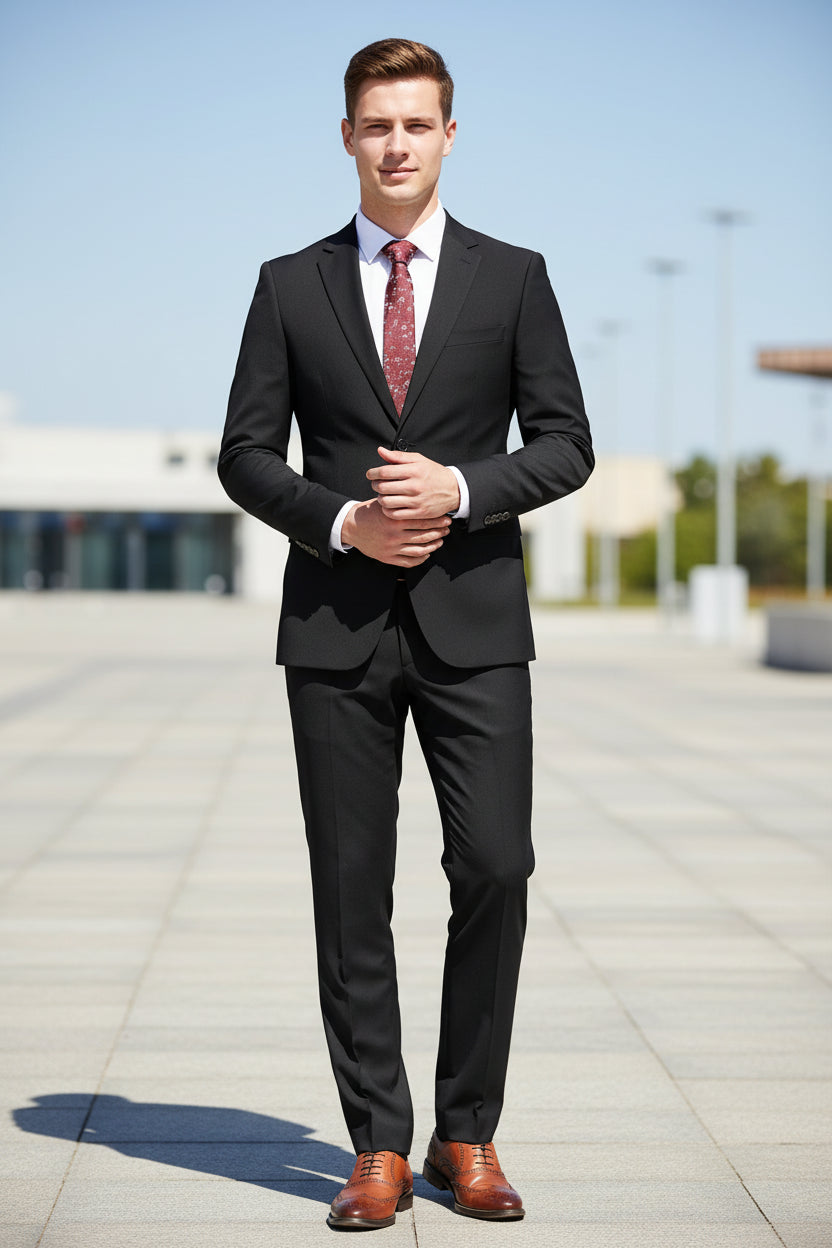 Black suit with a red patterned tie on a mannequin, paired with brown shoes on a white background.