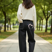 Black jeans with a pink heart design on the back pocket against a white background