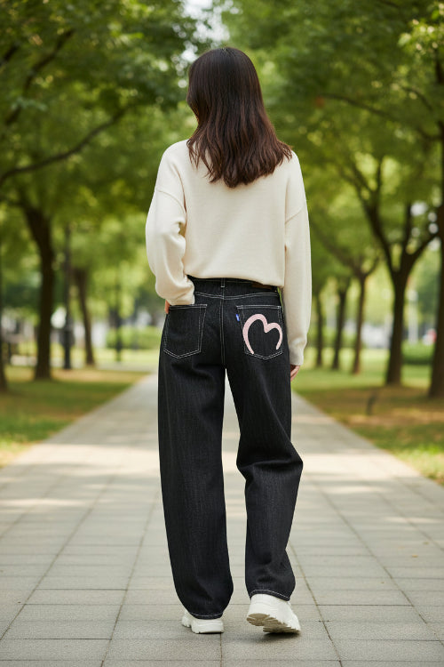 Black jeans with a pink heart design on the back pocket against a white background