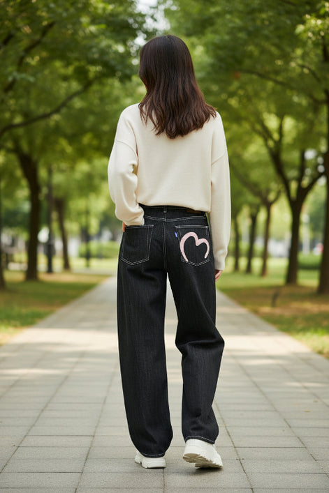 Black jeans with a pink heart design on the back pocket against a white background